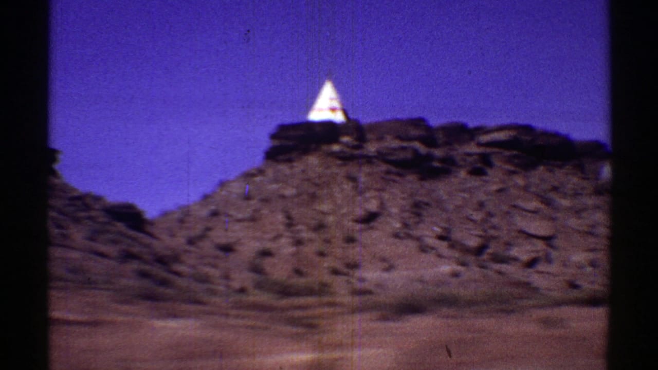 A white teepee stands above a rocky desert slope.
