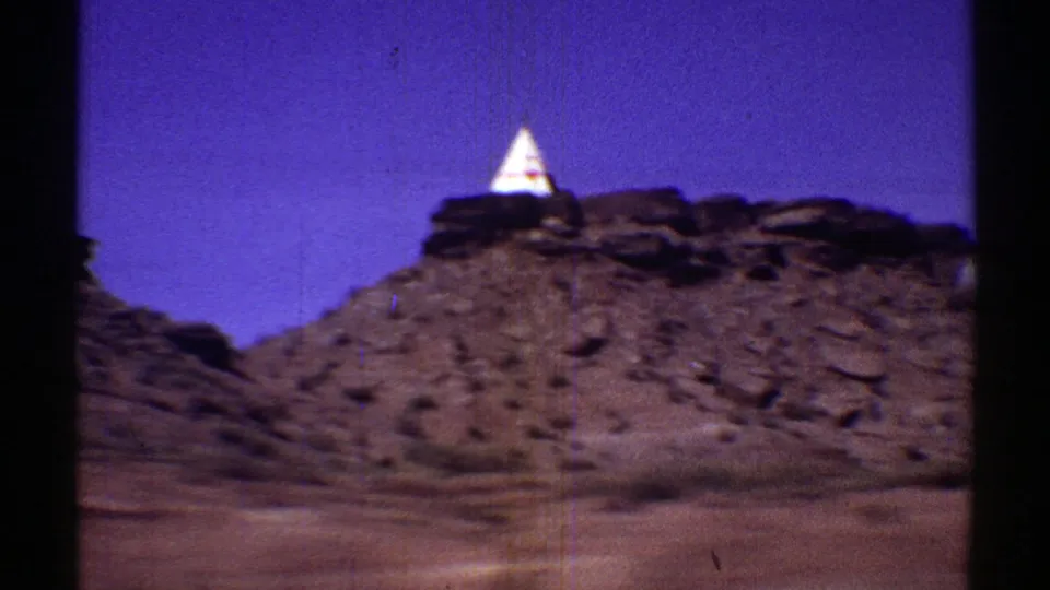 A white teepee-like roadside structure with red markings appears on a rocky Arizona desert slope in the 1969 footage.