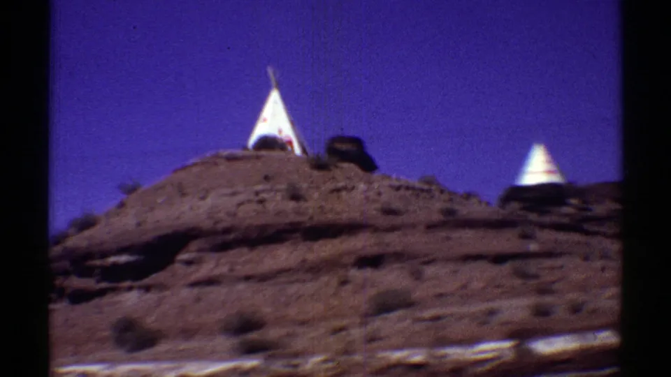 Two white teepee forms are partly visible behind a low rocky desert ridge in the Arizona road-trip footage.