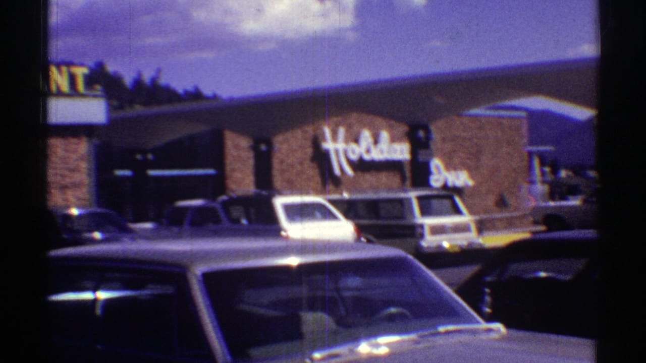 Holiday Inn and restaurant exterior with parked late-1960s cars under a bright sky.