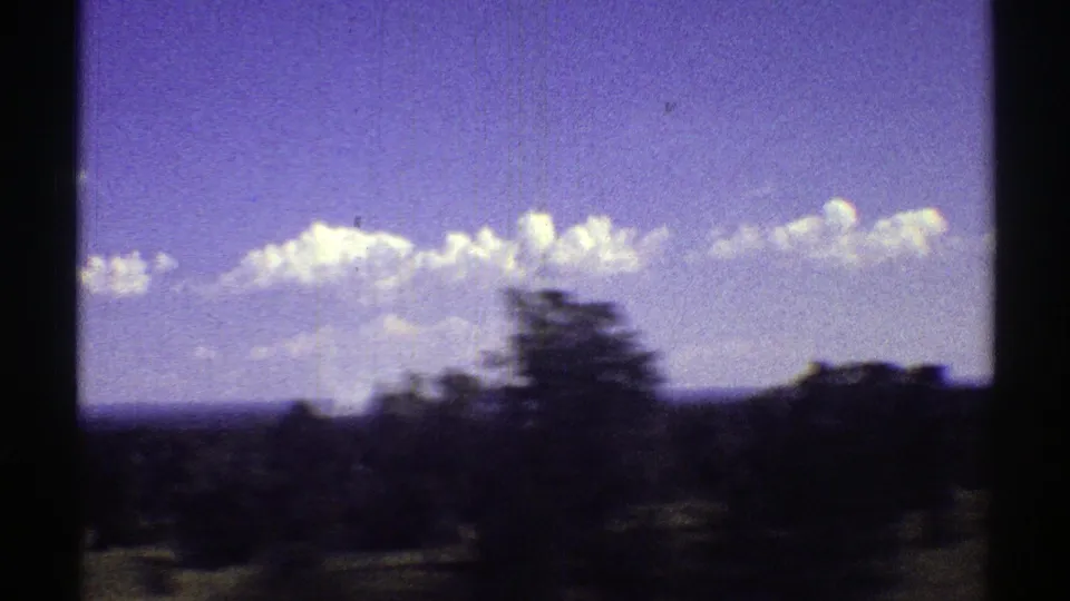 1969 Arizona roadside landscape frame with a blurred tree, low brush, distant horizon, and scattered white clouds on 8mm film.