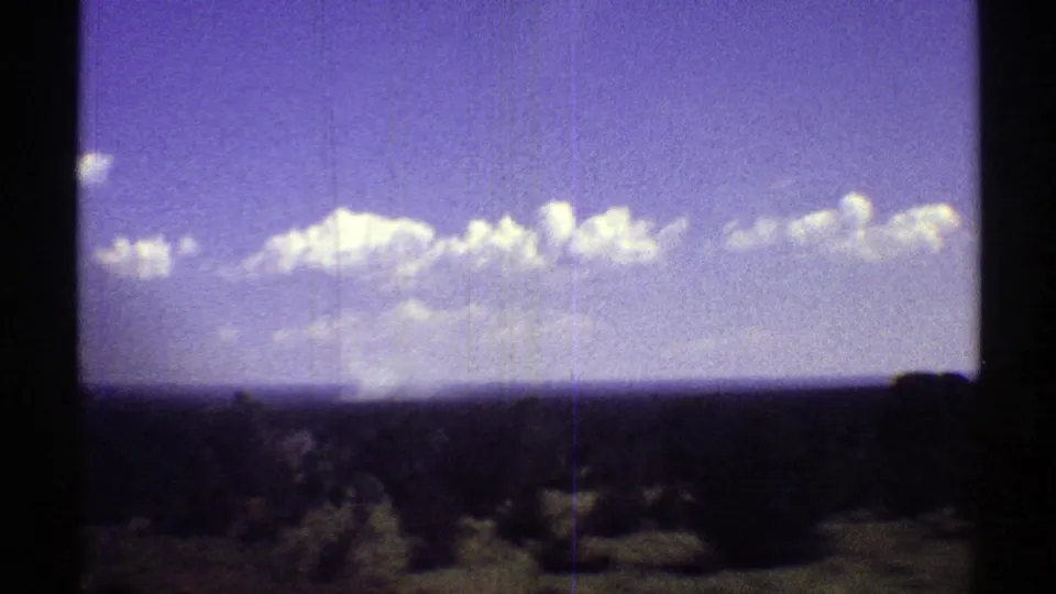 1969 Arizona 8mm frame showing open scrubland, distant horizon, and scattered clouds under a color-shifted sky.
