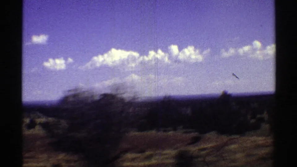 1969 Arizona travel-view frame with motion-blurred brush, wide horizon, and bright clouds across a purple-blue sky.