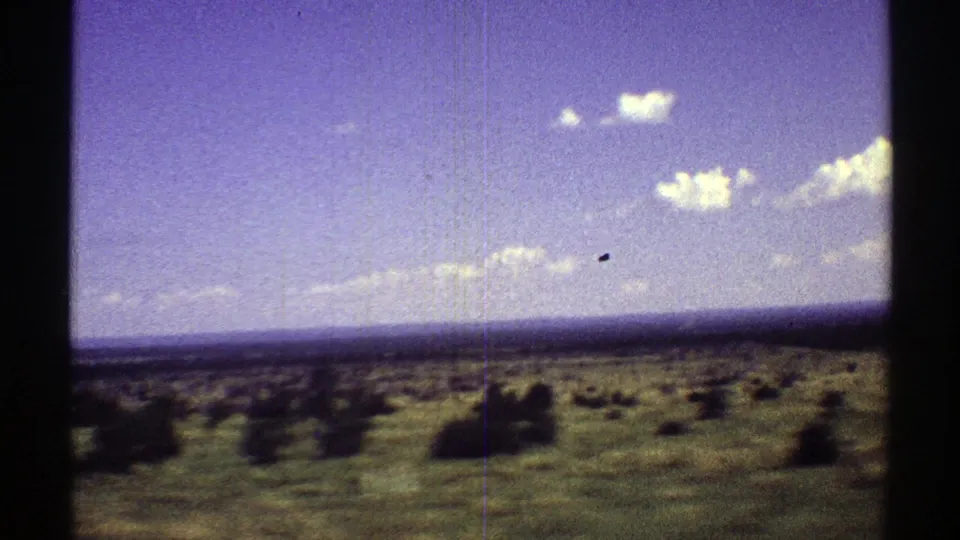 1969 Arizona home-movie frame showing low shrubs across open arid land beneath a blue-purple sky with scattered clouds.