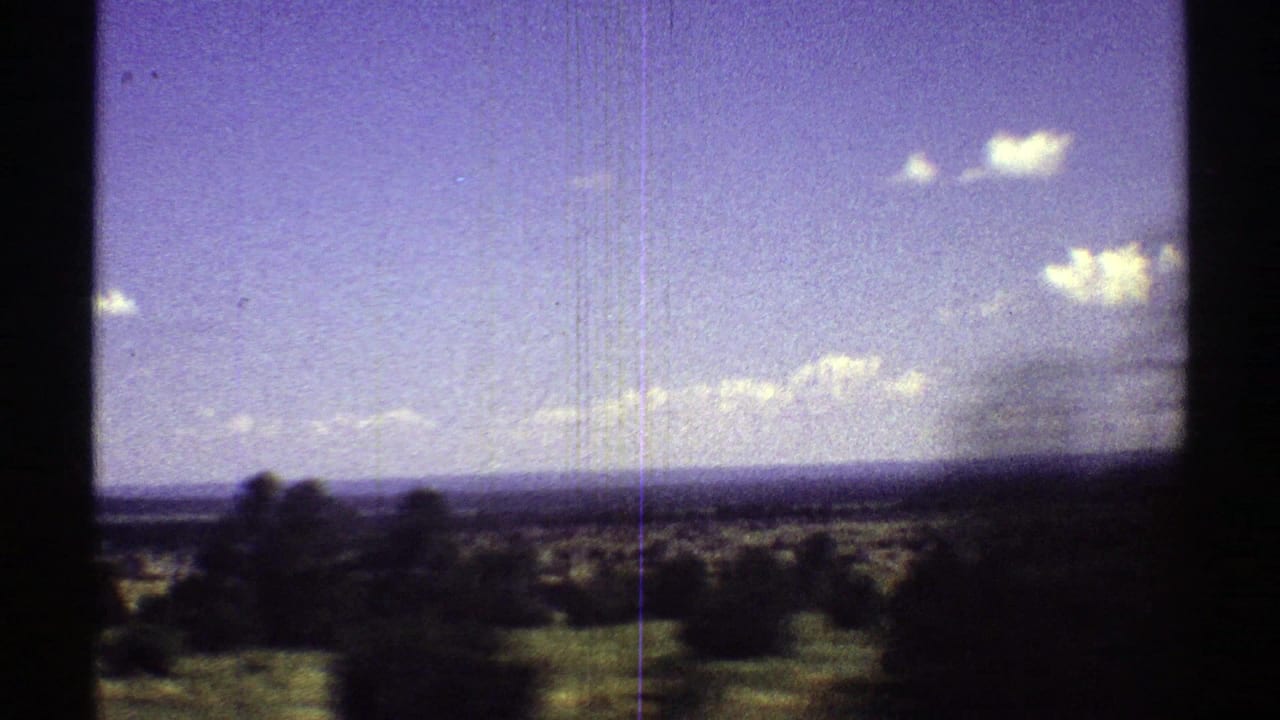 Distant open land with shrubs, a flat horizon, scattered clouds, and heavy dark frame borders.
