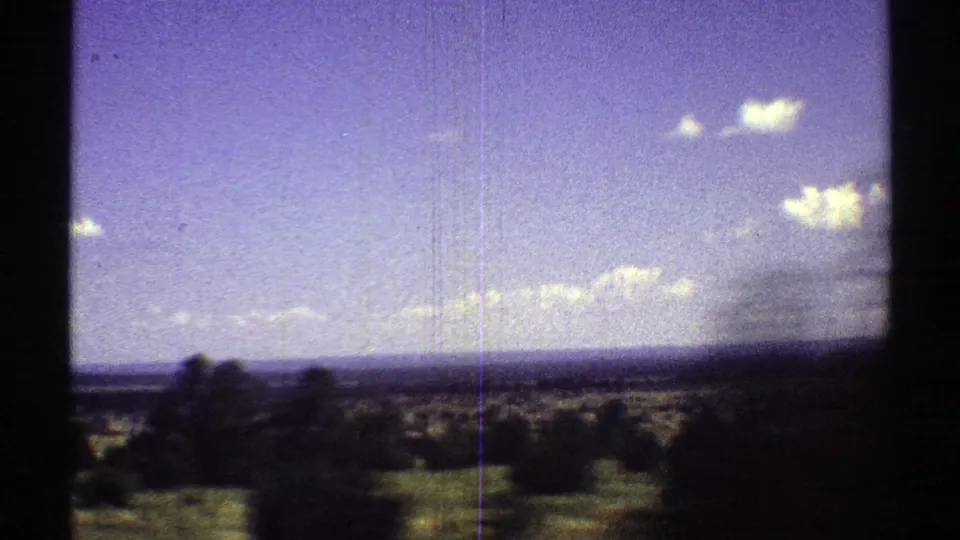 Arizona desert landscape in 1969 with scattered shrubs, a distant horizon, white clouds, and visible 8mm frame edges.