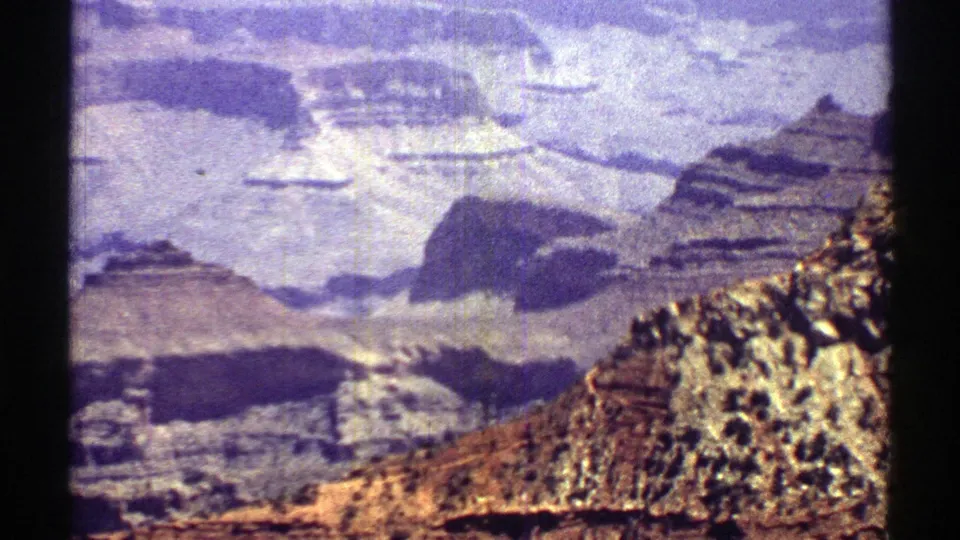 Aged 8mm frame from Arizona in 1969 showing a bright canyon overlook, pale rock terraces, and a sunlit rocky slope.