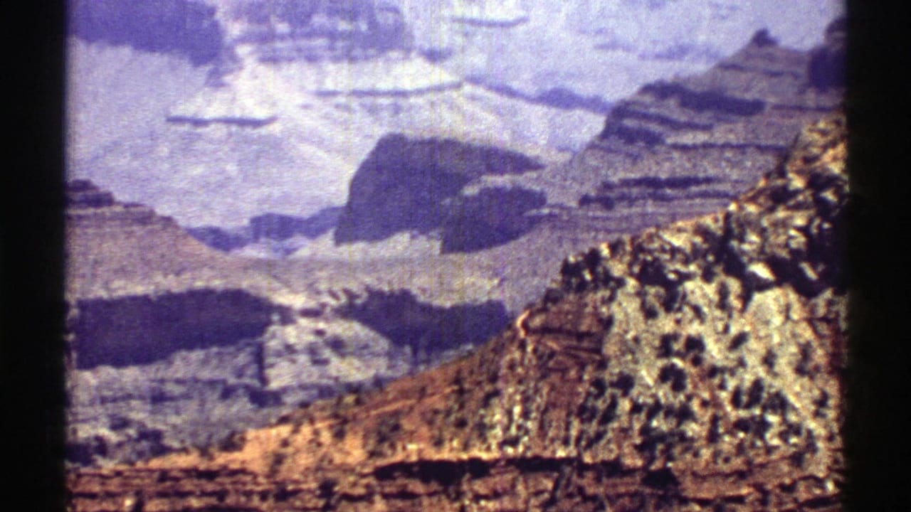1969 Arizona 8mm frame with stepped rock formations, distant canyon cliffs, and visible film grain.