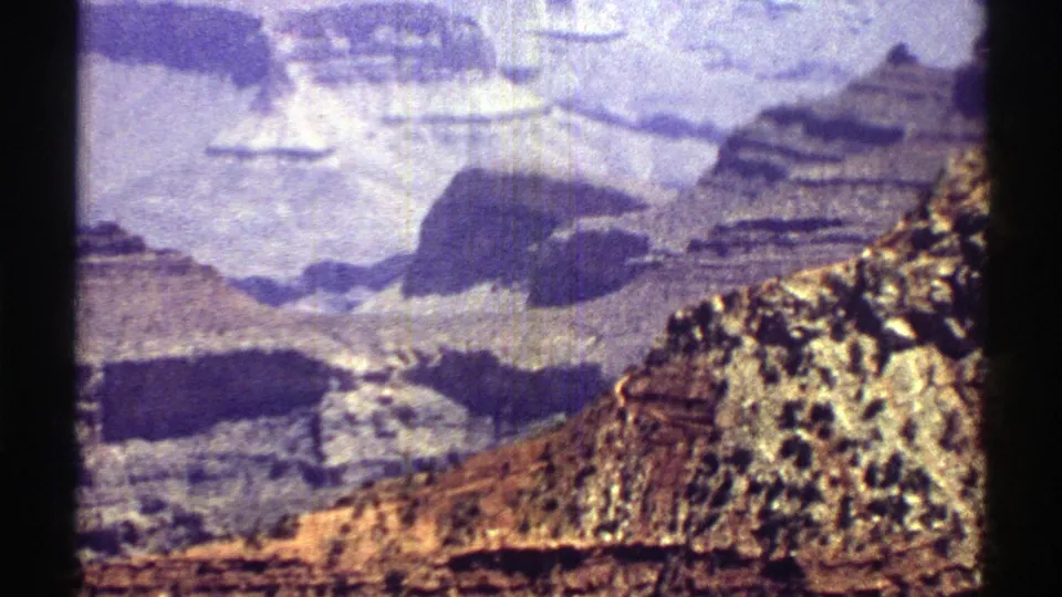 1969 Arizona 8mm frame showing a hazy canyon vista, shadowed rock layers, and a bright foreground ridge.
