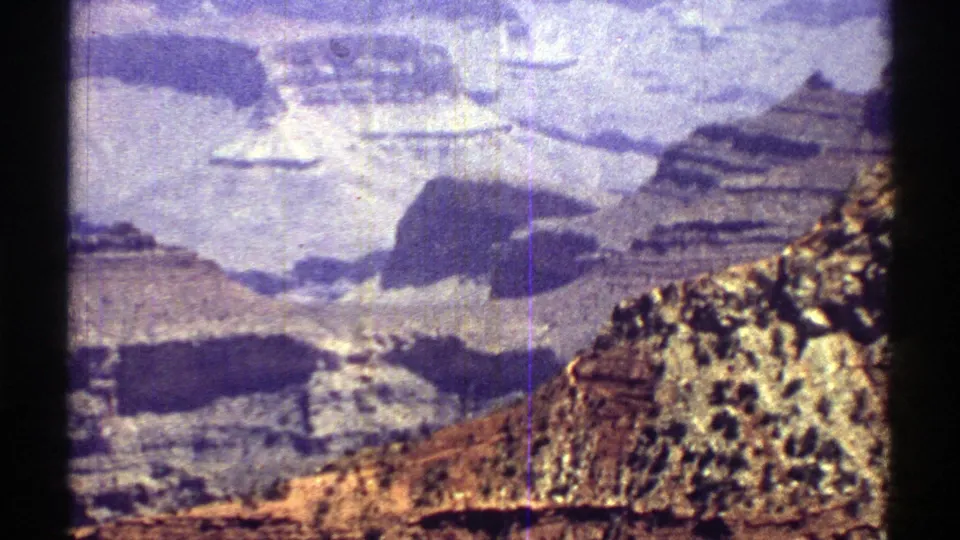 1969 Arizona 8mm frame showing rocky canyon slopes, distant cliff layers, and a vertical film scratch.