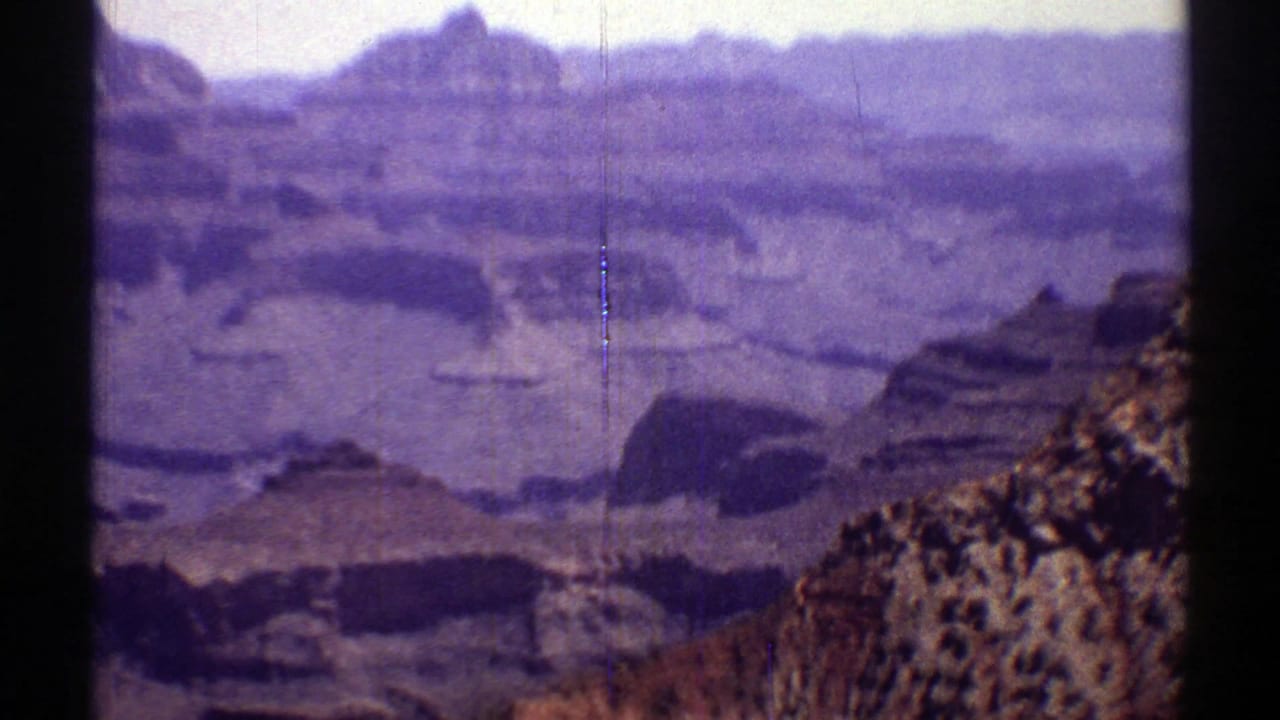 Layered canyon walls seen beyond a dark film-frame edge and rocky foreground.