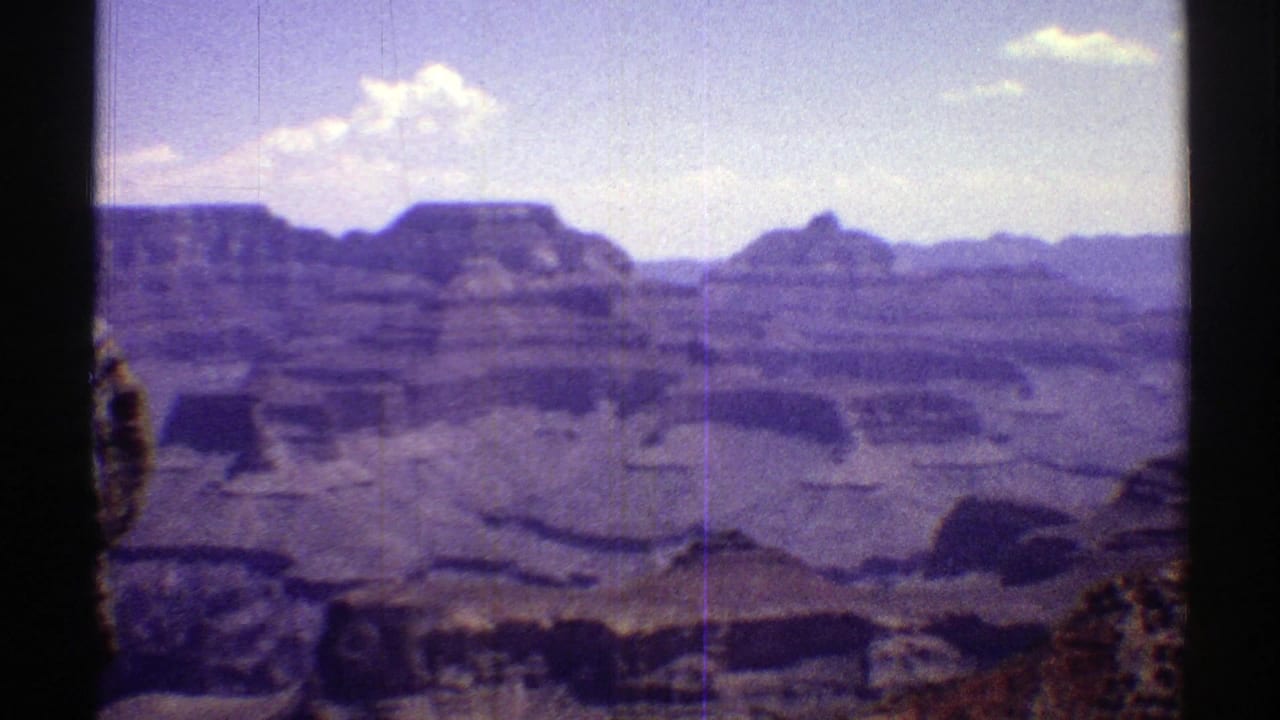 Vintage 8mm Arizona panorama showing distant mesas, layered canyon walls, shadowed ravines, and scattered clouds.