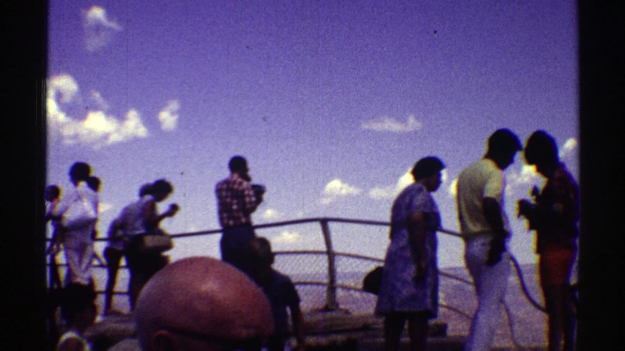Tourists stand behind a metal railing on a canyon viewing platform under a purple-blue sky.
