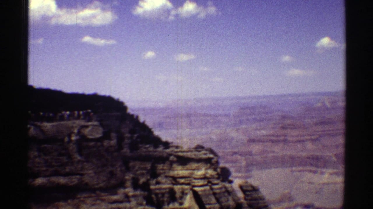 Grand Canyon rim and distant layered terrain appear in a 1969 Arizona 8mm frame with dark gate edges and saturated sky.
