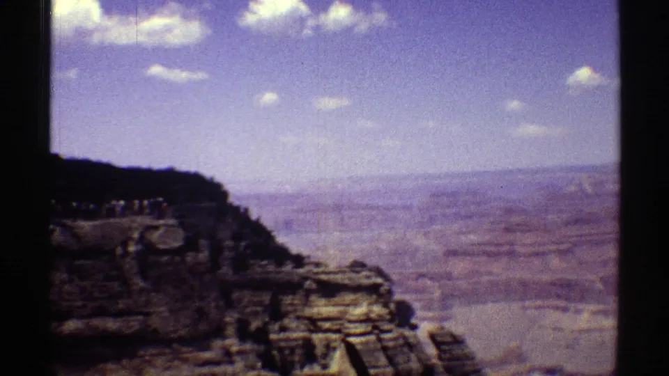 Grand Canyon rim and distant layered terrain appear in a 1969 Arizona 8mm frame with dark gate edges and saturated sky.