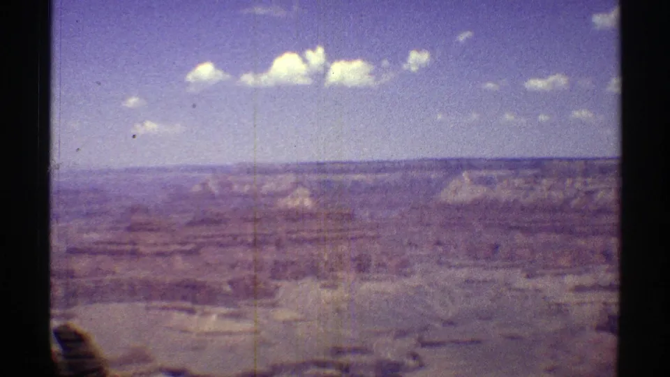 1969 Arizona Grand Canyon view with distant ridges, pale rock faces, scattered clouds, grain, and vertical film marks.