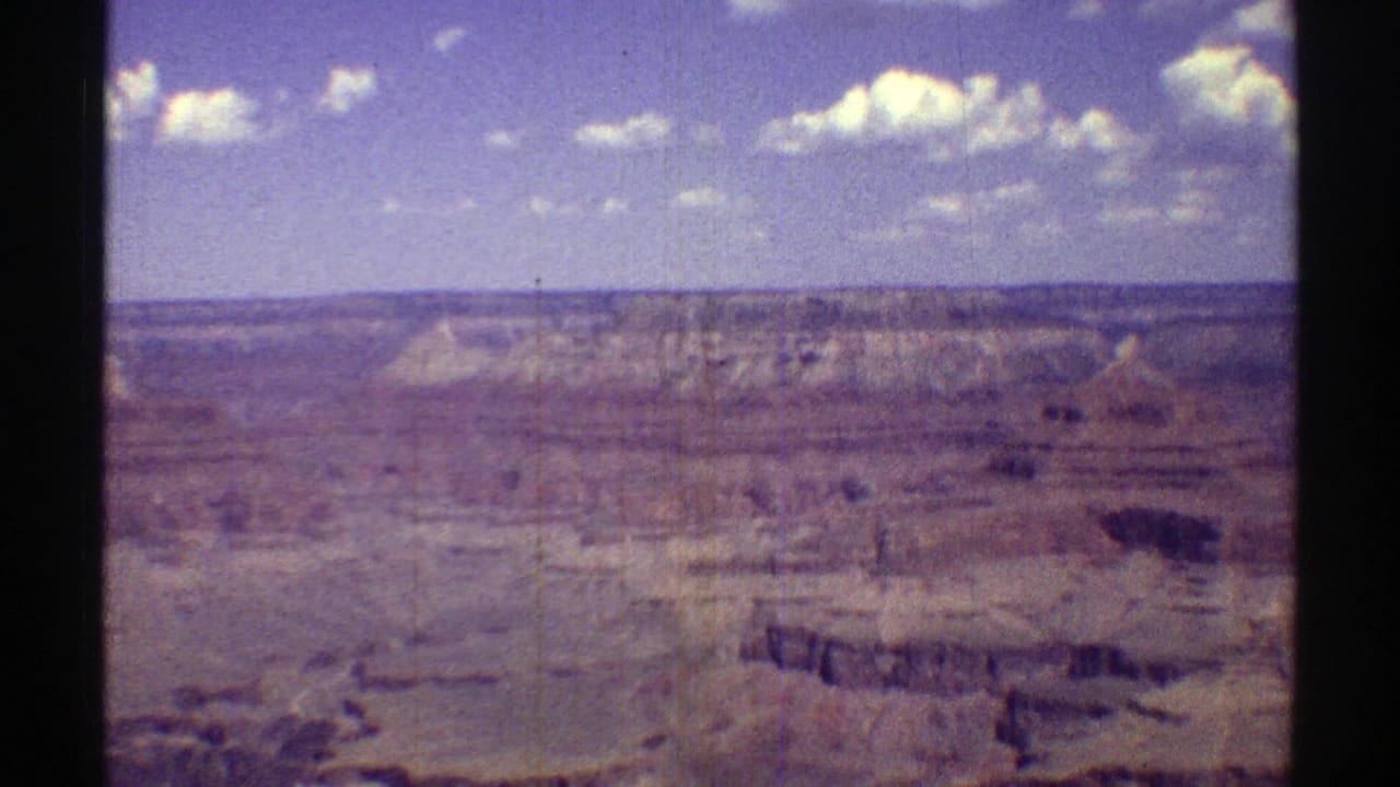 1969 Arizona home-movie frame with Grand Canyon cliffs, plateau edges, and cloud patches across the sky.