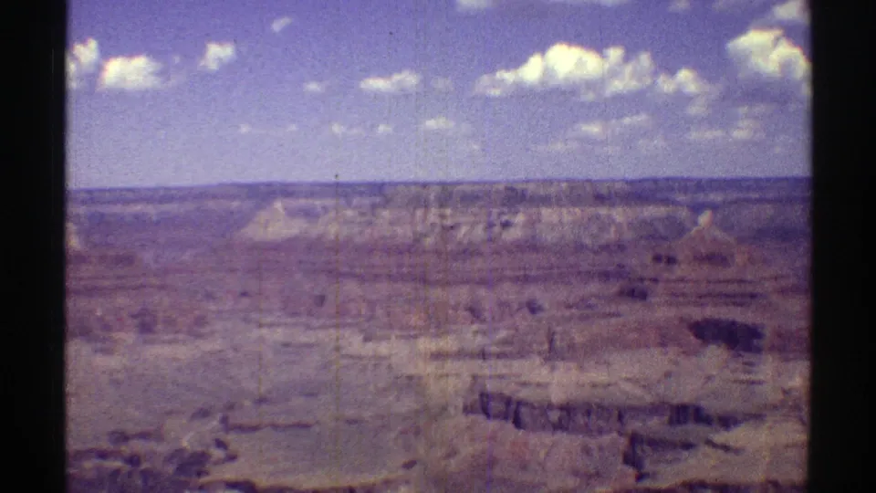 1969 Arizona home-movie frame with Grand Canyon cliffs, plateau edges, and cloud patches across the sky.