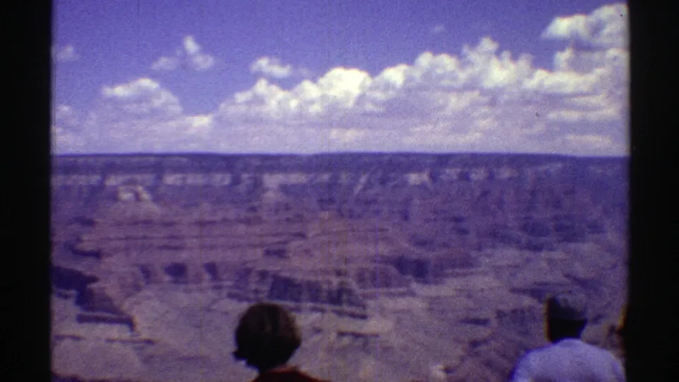 1969 8mm Arizona canyon overlook with two tourists partly visible against the expansive landscape.