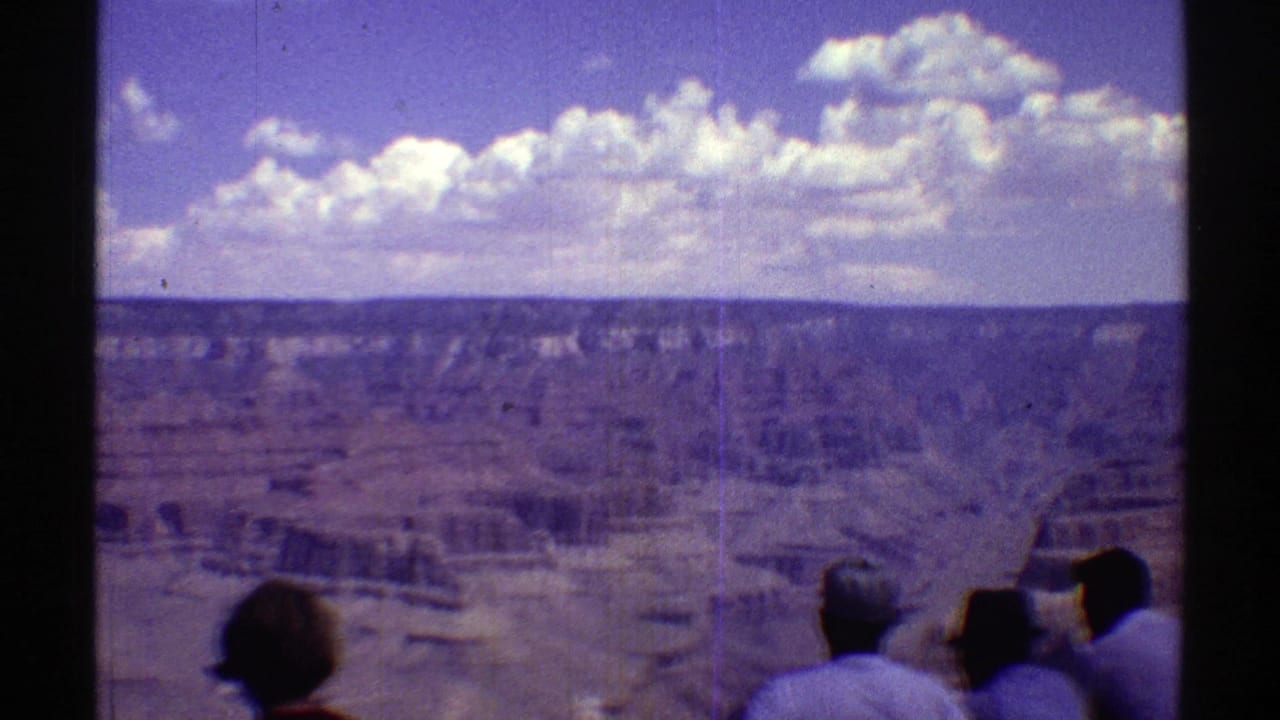 Visitors stand at a canyon overlook beneath a blue sky with white clouds.