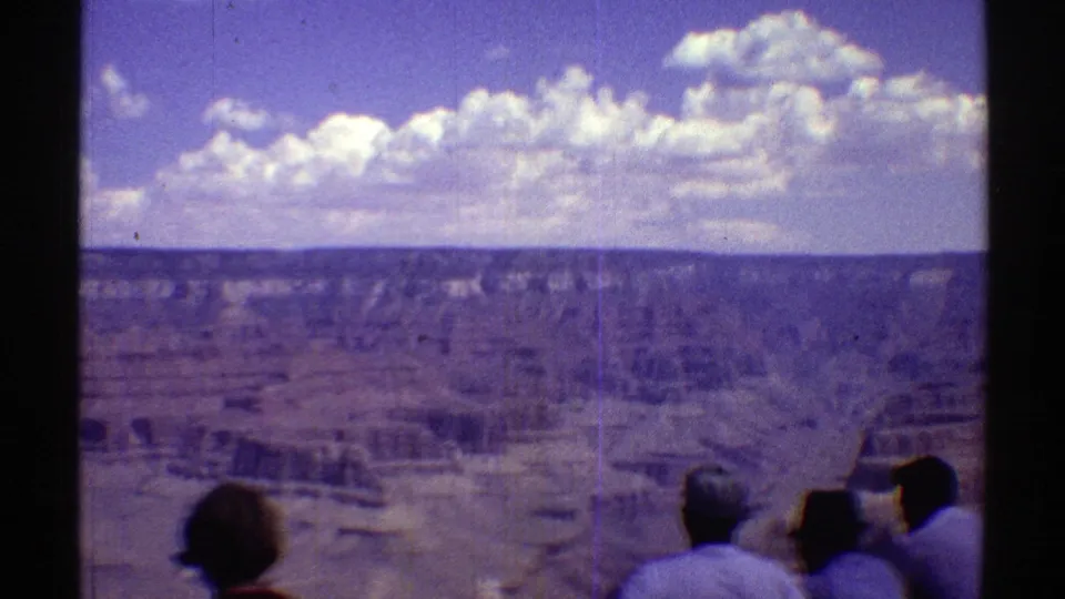 1969 Arizona home-movie frame of several visitors facing a broad desert canyon under scattered clouds.