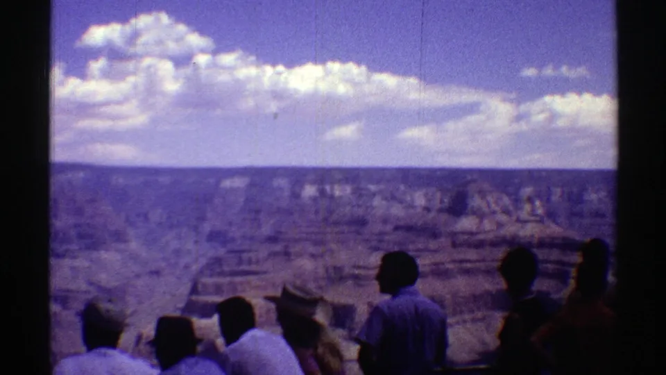 1969 Arizona 8mm frame showing tourists silhouetted against a layered desert canyon and bright clouded sky.