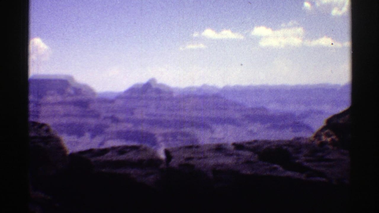1969 Arizona 8mm frame of a panning Grand Canyon vista with layered ridges and dark rocks in the foreground.