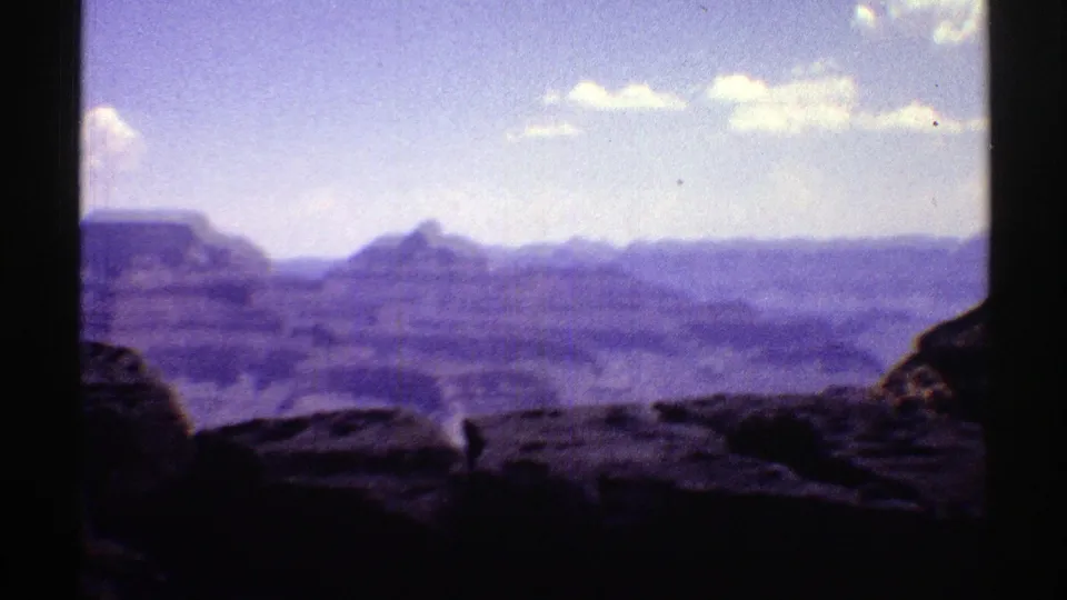 1969 Arizona 8mm frame of a panning Grand Canyon vista with layered ridges and dark rocks in the foreground.
