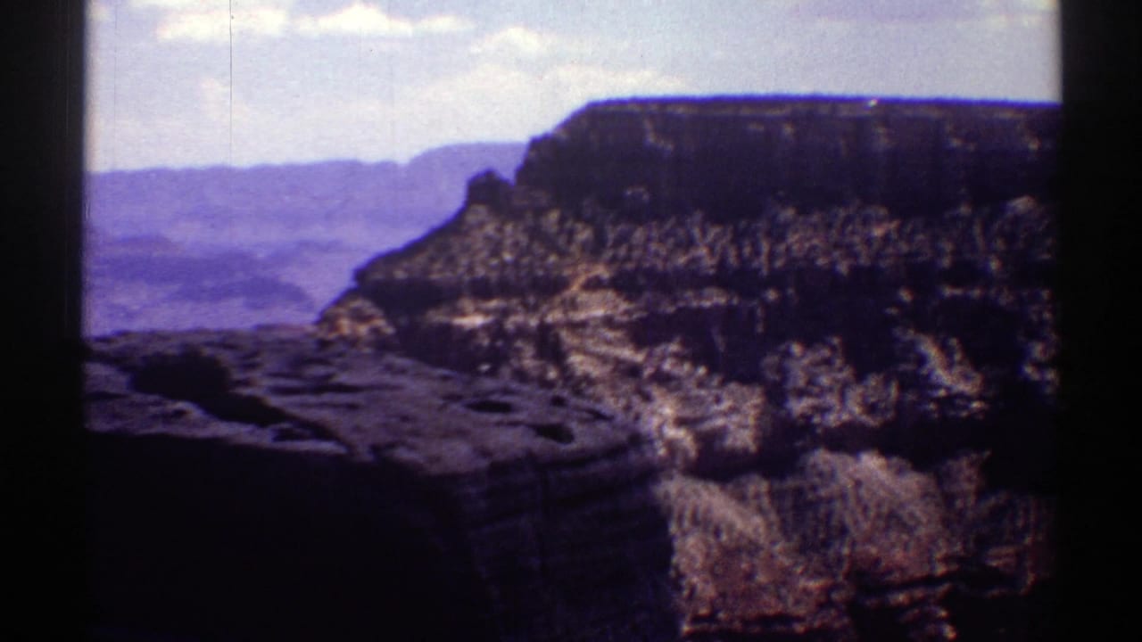 Wide canyon wall with layered rock and shadow under a pale sky.