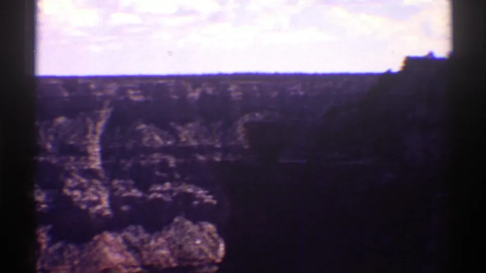1969 Arizona home-movie frame with a shadowed canyon foreground, bright sky, and visible rock layers along the left side.