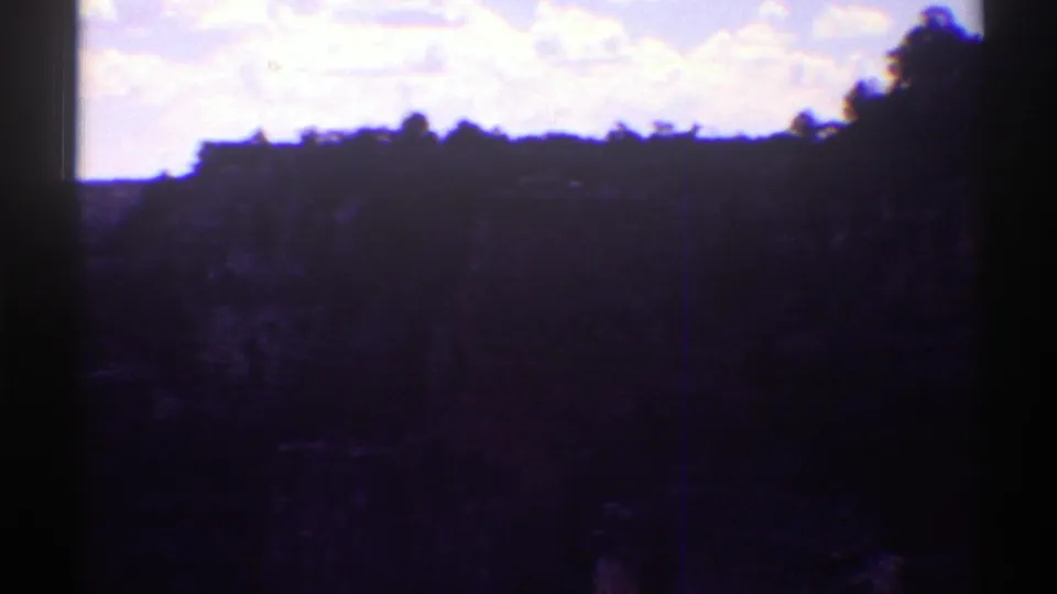 1969 Arizona 8mm frame showing a dark canyon rim or hillside silhouette beneath a bright sky, with heavy exposure shift and frame borders.