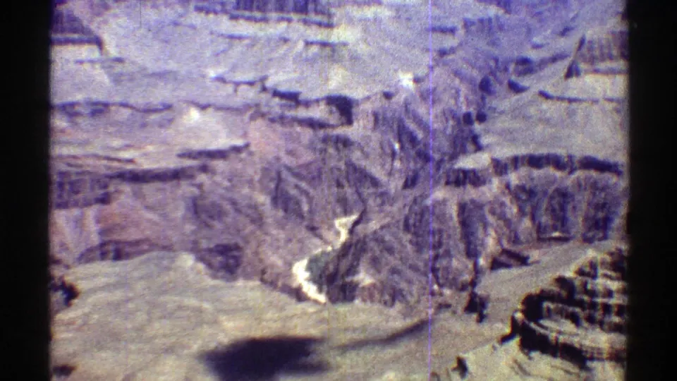 1969 Arizona 8mm frame showing striated canyon walls, pale stone ledges, and a dark aircraft or camera shadow crossing the foreground.