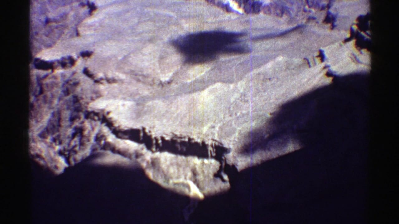 Wide desert terrain with pale flats, rugged ridges, dark shadows, and black film borders.