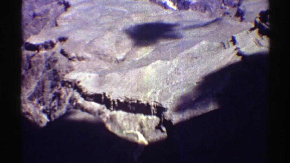 1969 Arizona 8mm frame showing a wide, sunlit desert basin with layered rocky ridges and heavy shadowing at the frame edge.