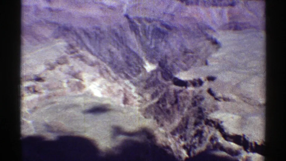 1969 Arizona 8mm frame showing rugged desert formations, pale open ground, and dark ridge shadows in a handheld home-movie view.