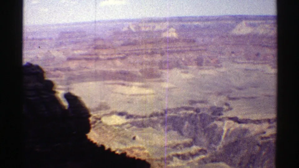 1969 Arizona 8mm vista with a shaded foreground cliff and layered canyon terrain beyond.