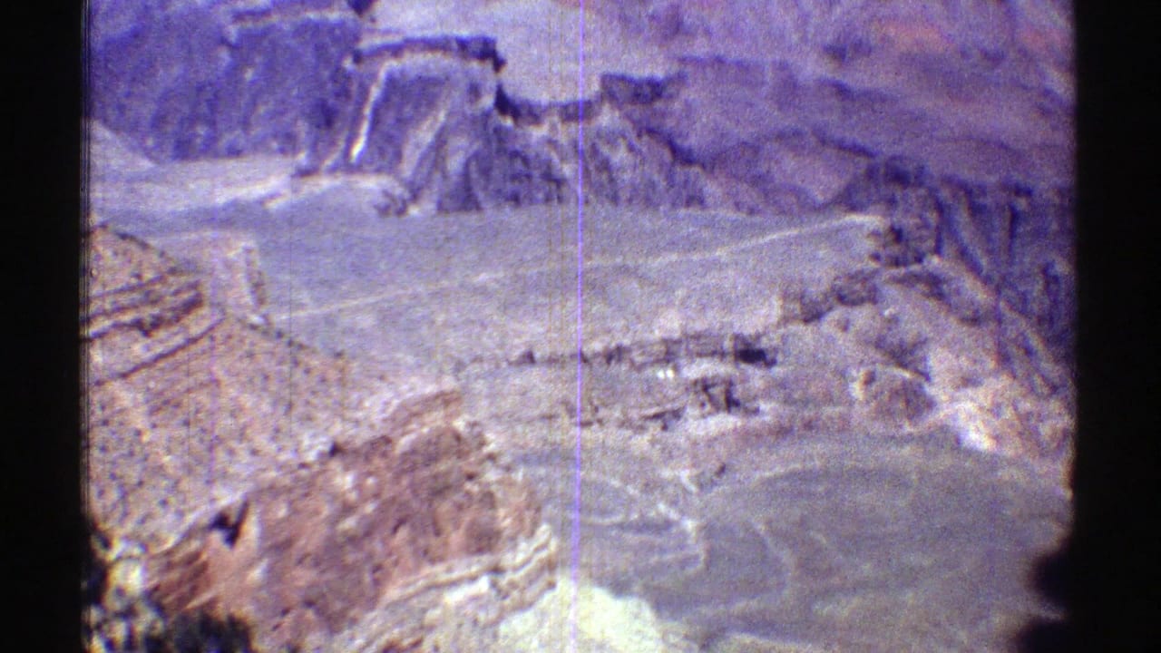 Aerial view over rocky desert mountains with a pale valley floor and road below.
