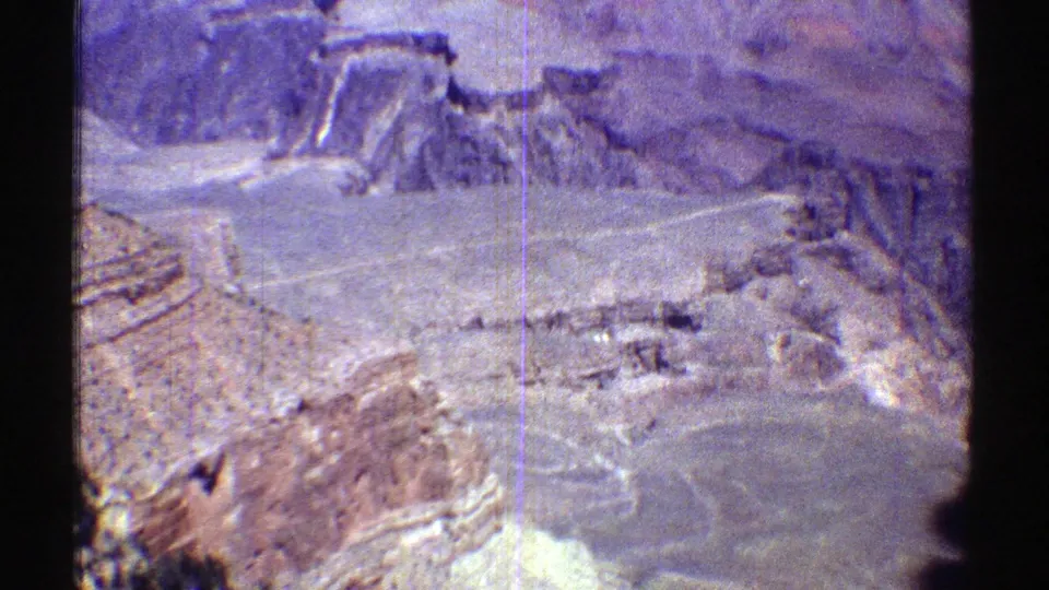 1969 Arizona 8mm aerial view showing rugged mountains, arid slopes, sparse vegetation, and a light road crossing the valley.