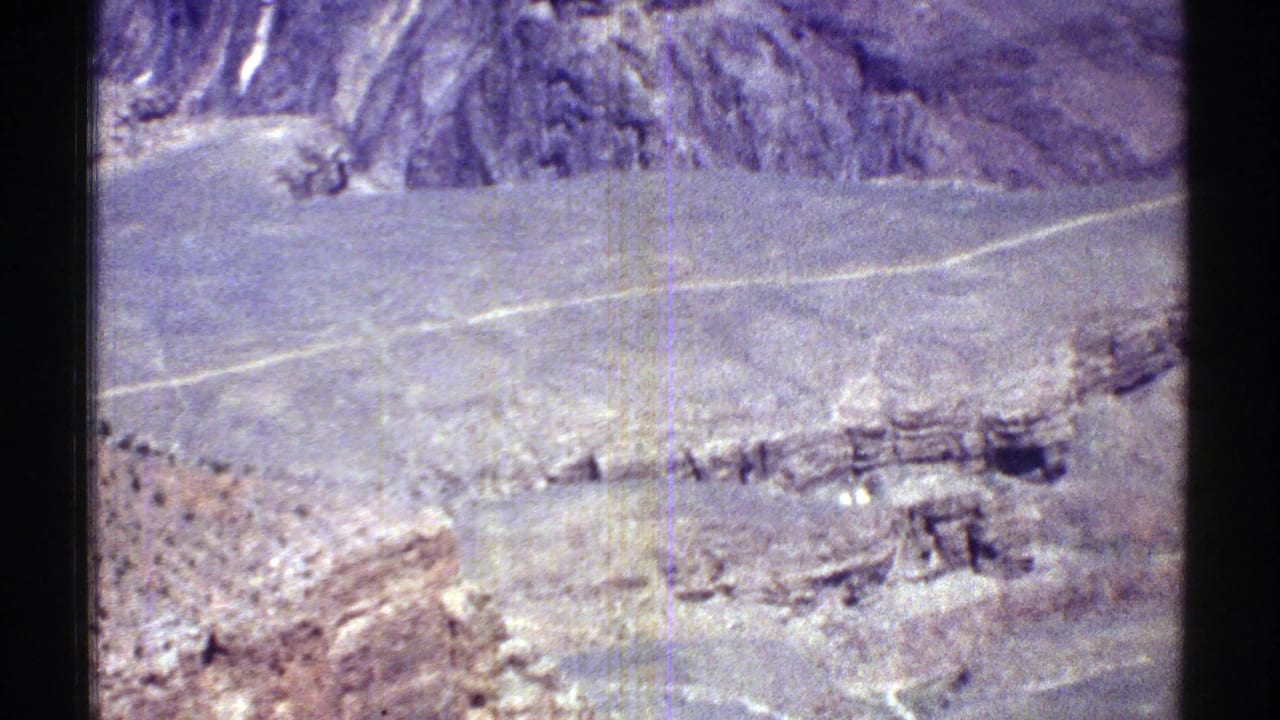 Rocky desert hillside and valley crossed by a pale road seen from above.
