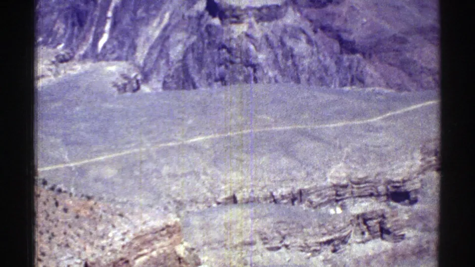 1969 Arizona home-movie frame showing a light road across arid highlands, with rocky ridges, scrub, and visible 8mm film wear.