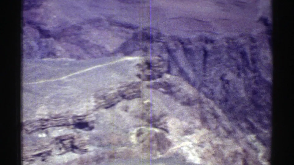 Arizona 8mm aerial frame with a winding pale road, steep rocky formations, dry ridges, and strong purple-blue film coloration.