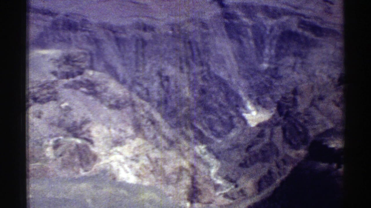 Rocky mountain terrain with pale slopes, shadowed ridges, and purple-grey film color shift.