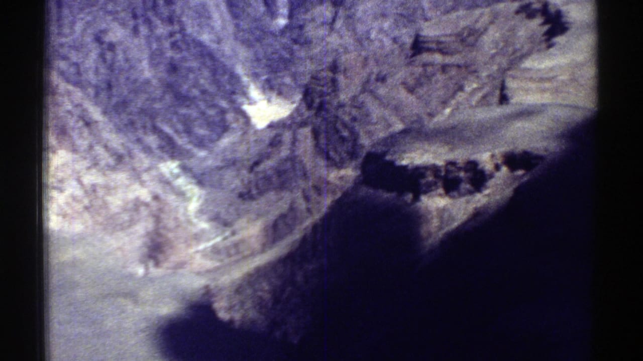 1969 Arizona 8mm view of steep grey-purple mountain terrain, with a dark shadowed foreground and visible film-frame edge.