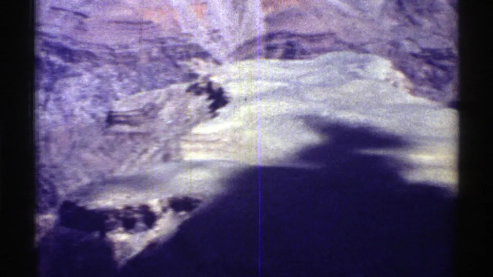 1969 Arizona home-movie frame showing a pale rocky mountainside, dark shadow, and visible 8mm scratches during the pan.