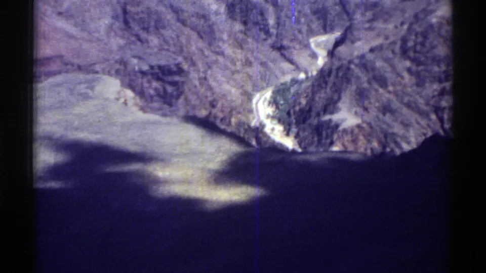 1969 Arizona 8mm frame showing a canyon-like rocky ridge, pale winding channel, and dark shadow across the lower frame.
