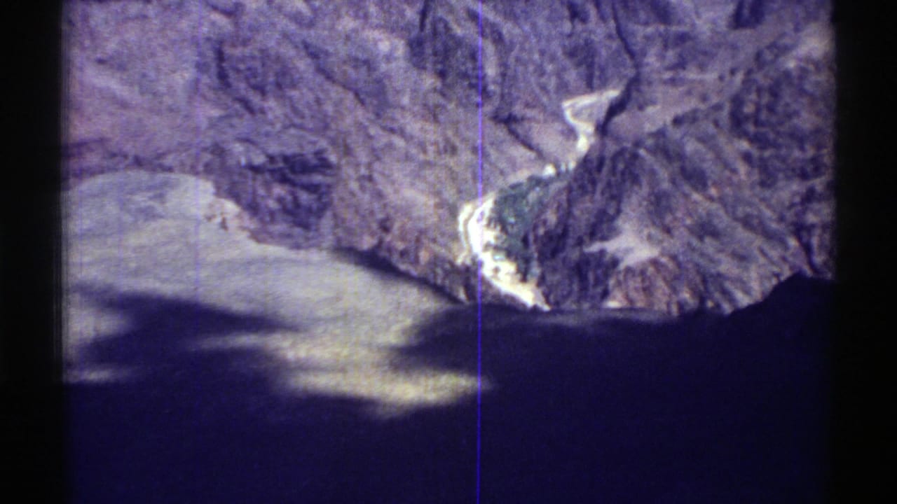 1969 Arizona 8mm aerial view over rugged canyon terrain, dark water, pale rock, and purple-blue film color shift.