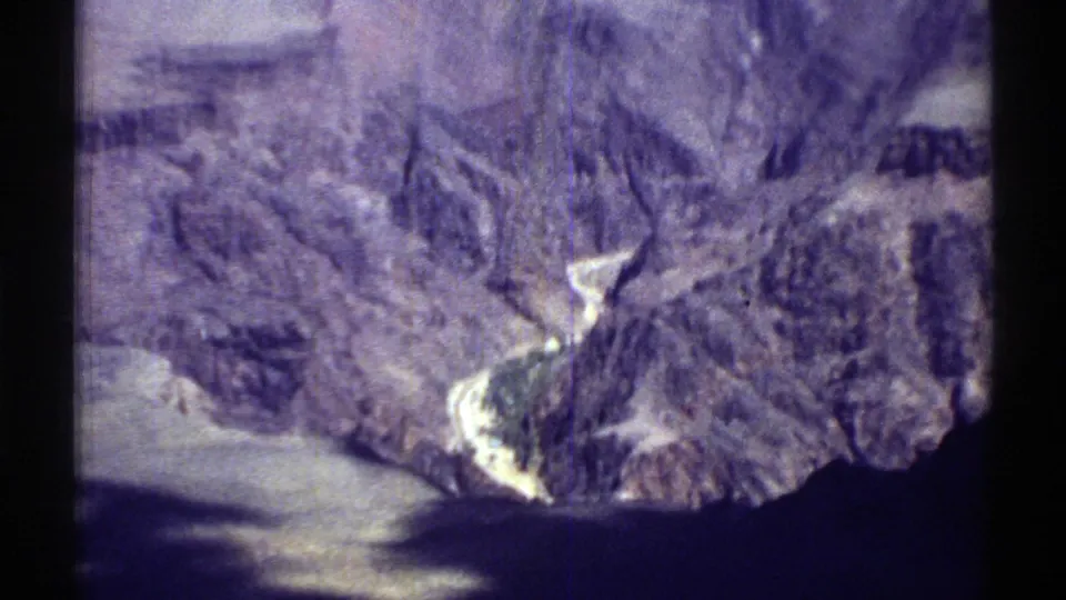 Aerial home-movie frame showing Arizona canyon rock, shoreline contrast, and a winding water edge in soft 8mm color.