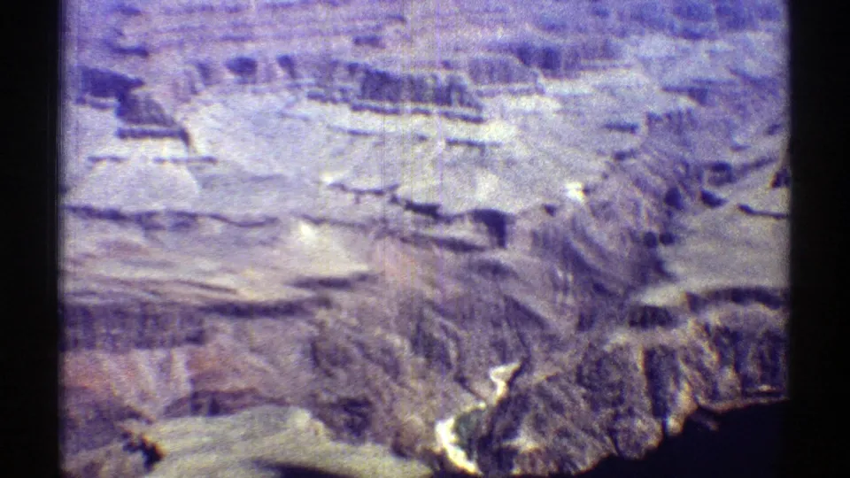 1969 Arizona aerial frame with layered canyon formations, pale rock shelves, and a partial dark water edge at the lower frame.