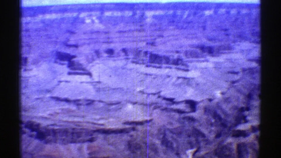 Aerial 8mm view over Arizona canyon terrain with strong blue-purple color shift, pale rock surfaces, and dark water along the frame edge.