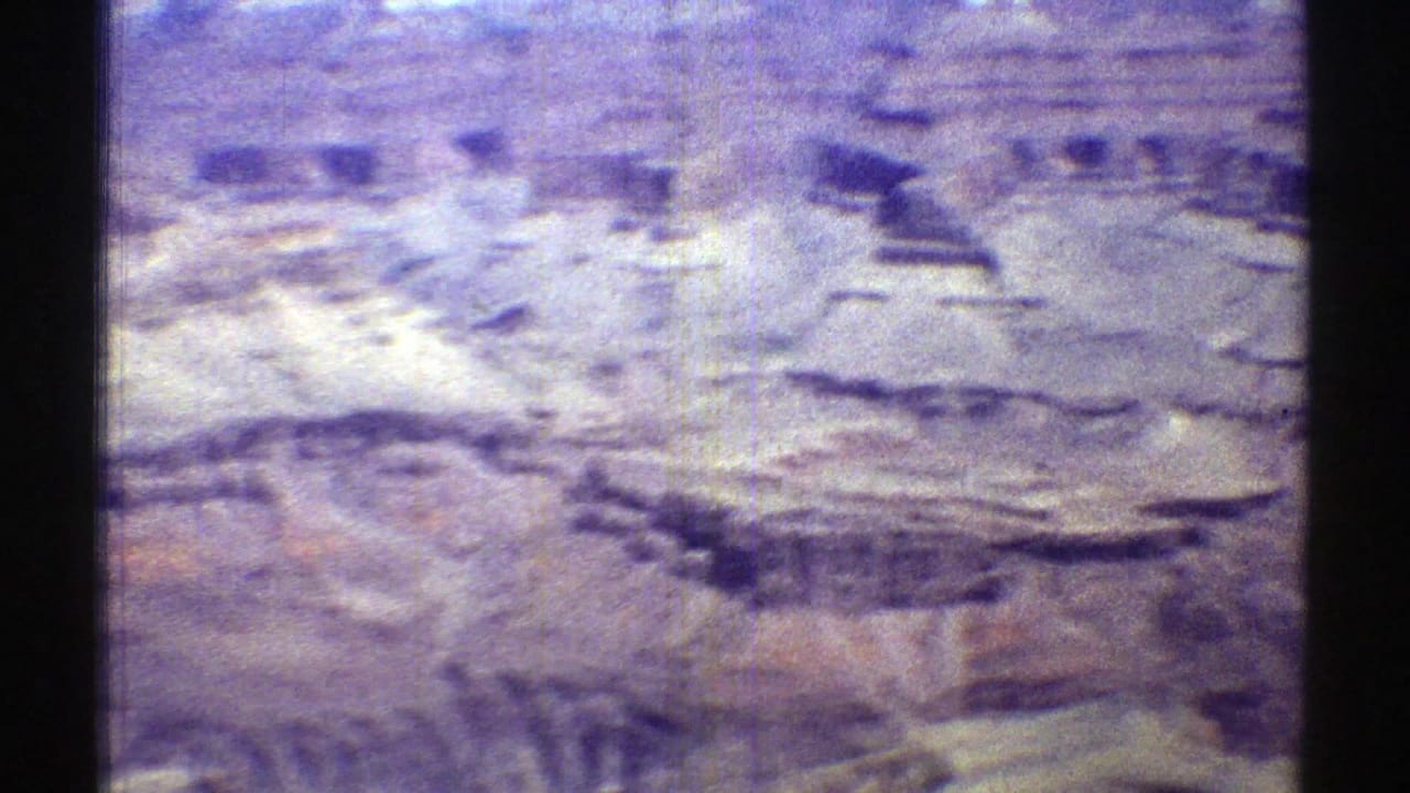 Aerial view of pale and reddish mesa rock with canyon cuts and aged purple film color.
